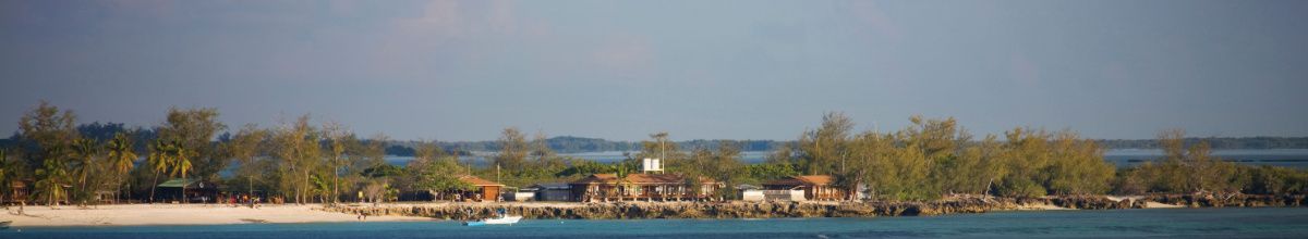 Ein Strand auf Aldabra mit einigen Hütten und Vegetation bei Tag.