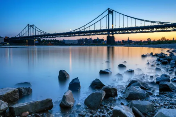 Brücke über den Rhein Eine alte Brücke über den Rhein in Krefeld mit einem Steinstrand bei Sonnenuntergang.