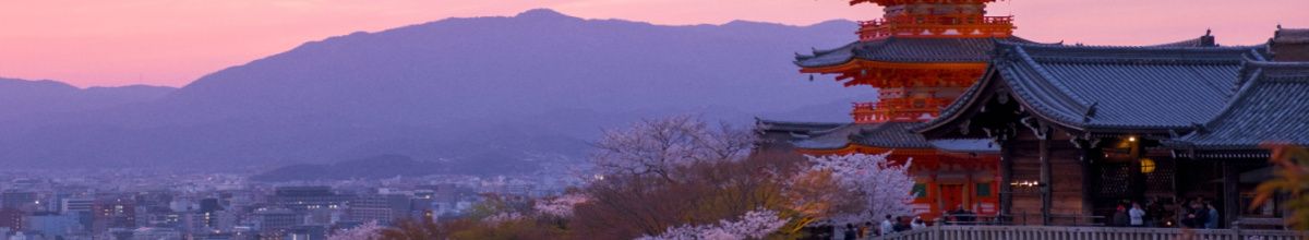 Kyoto in der Dämmerung mit einem großen, roten Tempel und Bergen im Hintergrund.