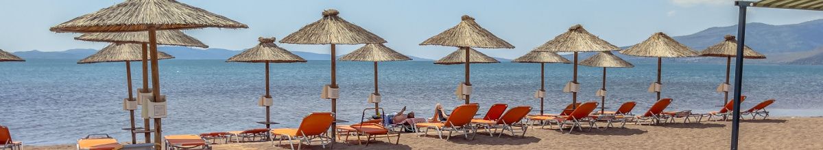 Ein Sandstrand auf Lesbos mit einigen Sonnenschirmen und dem ägäischen Meer im Hintergrund bei Tag.