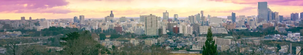 Ein Panorama der Stadt Sendai bei Sonnenuntergang gespickt mit Wolkenkratzern, Parks und der urbanen Stadtlandschaft.