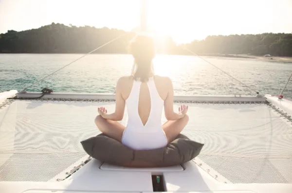 Frau sitzt im Schneidersitz auf Segelboot und wird von der Sonne angeschienen.