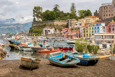 Ausschnitt des Hafens von Marina Grande mit ausrangierten Ruderbooten und den bunten Hausfassaden des Ortes bei Tag.