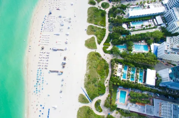 Der Strand von Miami an einer überwachsenen Strandpromenade und Hochhäusern mit Pools von oben.
