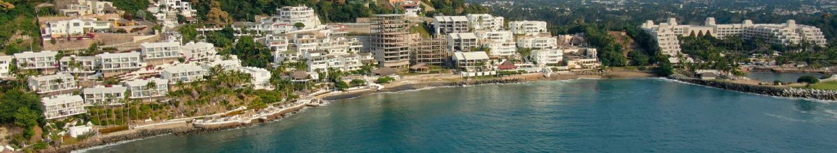 Luftaufnahme der Hafenkante von Manzanillo bei Tag mit den Häusern der Stadt und dem Meer.