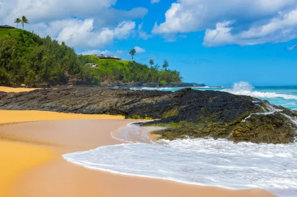Der geheime Strand (Kauapea Beach) mit hellem Sand und Palmen im Hintergrund.