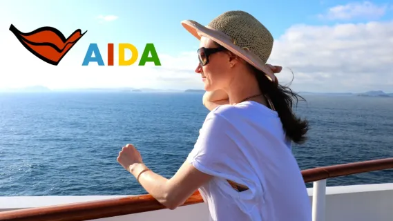 Eine junge brünette Frau steht an der Reling eines Kreuzfahrtschiffes und blickt auf das Meer. In der linken oberen Ecke das AIDA Logo mit rotem Kussmund und AIDA Schriftzug in blau, rot, gelb, grün.