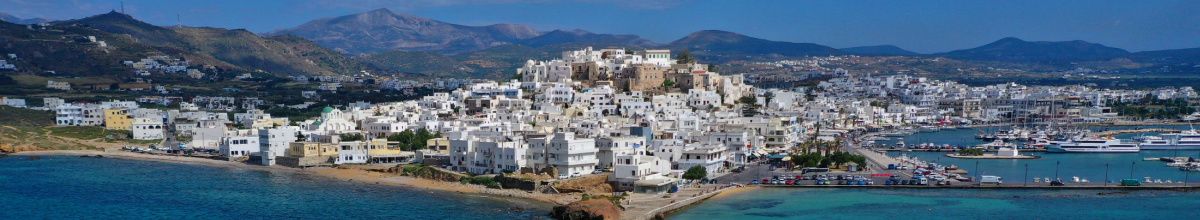 Eine Totale der Stadt Naxos am Tag mit den weißen Hausfassaden der Stadt im Mittelpunkt.