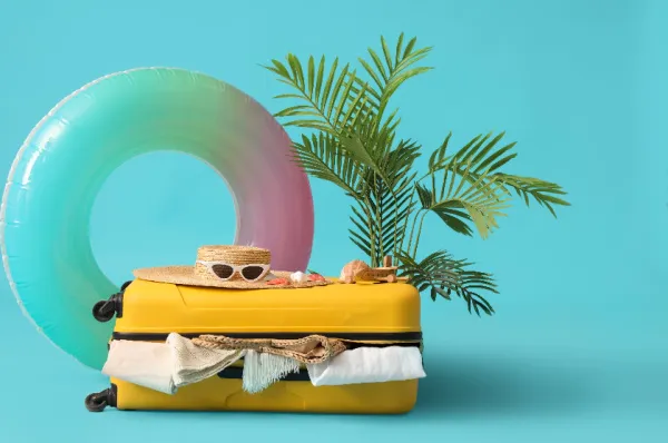 Geld sparen außerhalb der Saison, ein Artwork mit Koffer, Schwimmreif und Badeuntensilien.