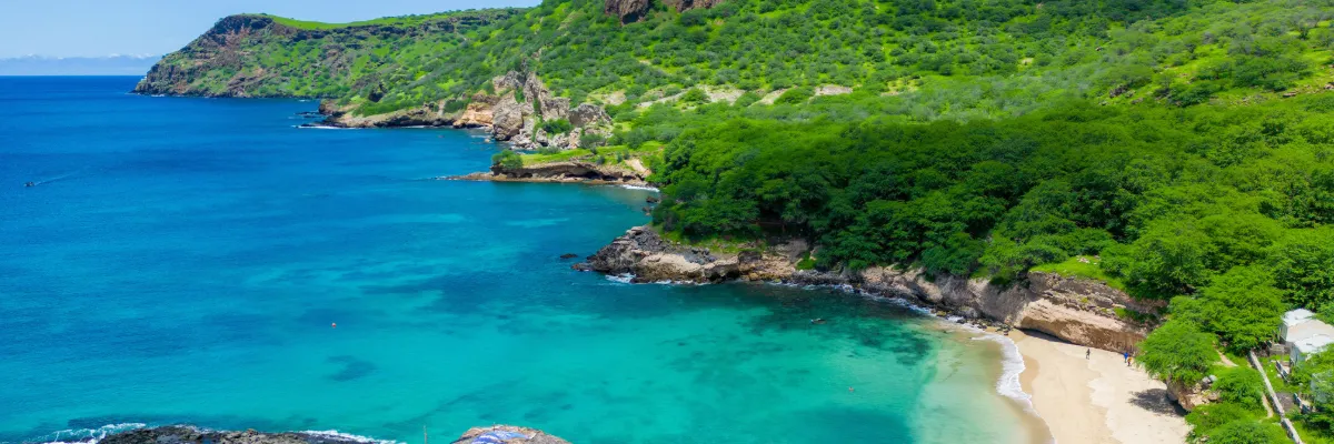 Traumhafter Strand mit türkisfarbenem Meer und weißem Sand vor einer grünen Palmenlandschaft.