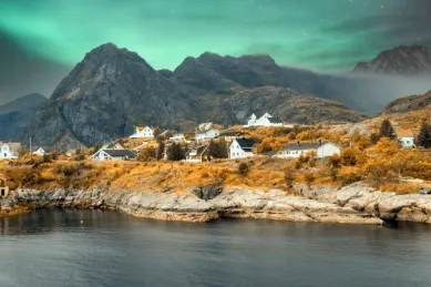 Grüne Nordlichter über Harstad, mit Bergen im Hintergrund.