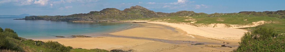 Ein kleiner Sandstrand auf Colonsay bei Tag mit felsigen Hügeln im Hintergrund.