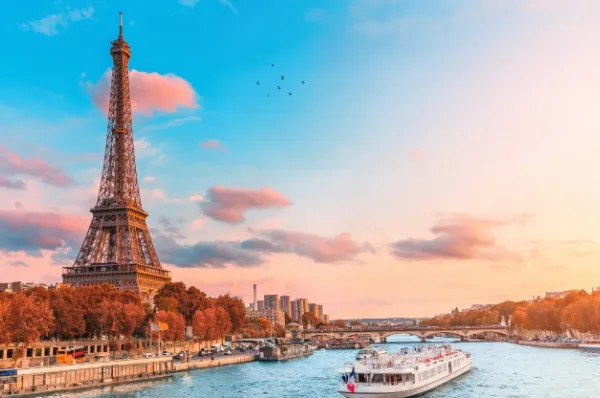 Der Eiffelturm in Paris bei leichtem Sonnenuntergang und einem Schiff auf der Seine.