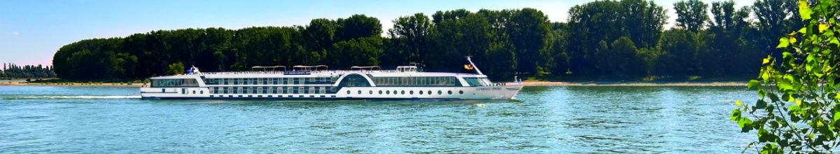 Die MS COMPASS OPERA fährt entlang eines bewaldeten Flussufers.