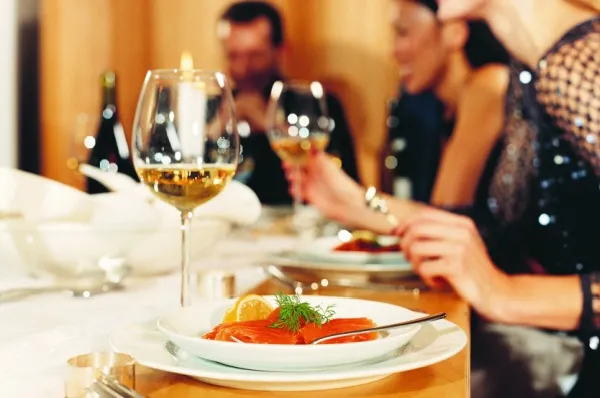 Personen sitzen gemeinsam beim Dinner, auf dem Teller ist ein Stück Lachs und vor dem Teller stehen Weißweingläser.