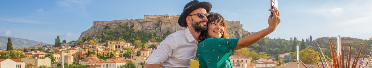 Ein glückliches Paar macht ein Selfie mit dem Smartphone vor der historischen Akropolis in Athen während eines Landausflugs mit Norwegian Cruise Line.