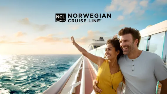 NCL Free at Sea – Sorgenfreies Freestyle Cruising erleben Ein lächelndes Paar steht Arm in Arm an der Reling eines Norwegian Cruise Line Kreuzfahrtschiffs und blickt bei Sonnenuntergang auf das weite Meer.
