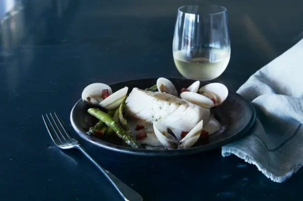 Ein Meeresfrüchteteller und ein Glas Weißwein stehen auf einem Tisch, daneben liegt eine Gabel und eine Stoffserviette.
