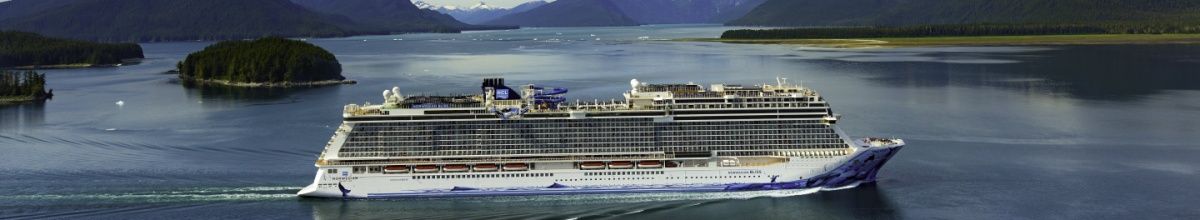 Die Norwegian Bliss auf dem Meer, im Hintergrund Berge und grüne Natur.