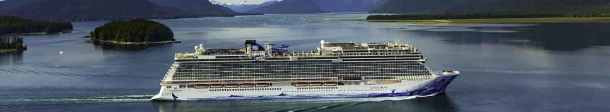 Die Norwegian Bliss auf dem Meer, im Hintergrund Berge und grüne Natur.