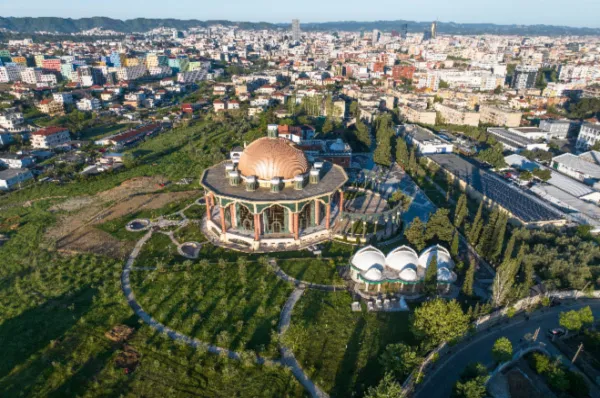 Vogelperspektive auf das Bektashi World Headquarter am Saum von Tirana inmitten eines Parks, mit der Großstadt im Hintergrund bei Tag.