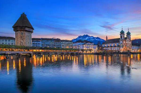 Die Hafenkante von Luzern am Abend mit warmen Lichtern der Stadt, welche sich auf dem Wasser brechen.