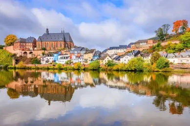 Blick auf Saarburg am Fluss Saar mit einer Kapelle und kleinen Häusern am Ufer.