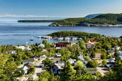 Luftaufnahme des Ortes Tadoussac inmitten grüner Natur und unmittelbar am Wasser gelegen bei Tag.