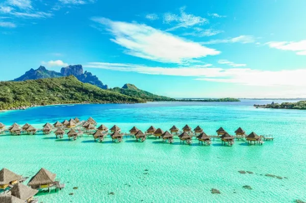 Luftaufnahme einer Lagune auf Bora Bora mit kleinen Wasserhütten an einem Steg.