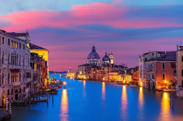 Historische Handelsrouten im Mittelmeer: Auf den Spuren von Entdeckern in Venedig Der Canal Grande in Venedig bei Dämmerung mit beleuchteten Palästen und der Kuppel der Kirche Santa Maria della Salute im Hintergrund, Symbol für historische Mittelmeer-Kreuzfahrten.