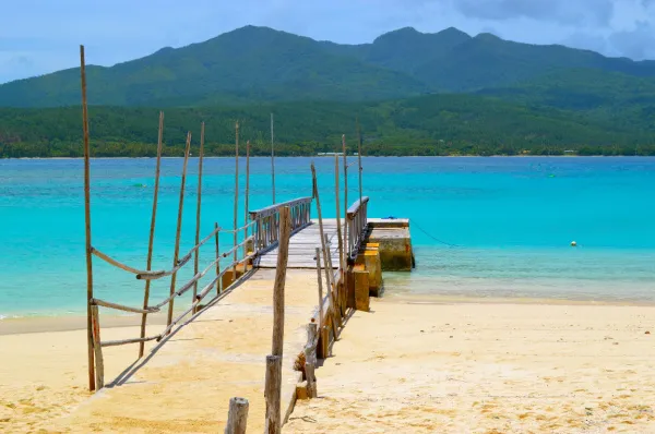 Ein Steg auf Mystery Island Ein einsamer Steg, der ins Wasser ragt auf Mystery Island am Tag mit einer Nachbarinsel im Hintergrund.