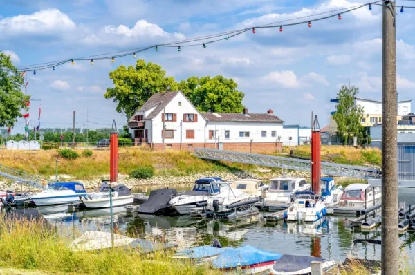 Ein Teil des Hafens von Gernsheim mit einem Fachwerkhaus, grünen Wiesen und kleinen Speedbooten am Ufer bei Tag.