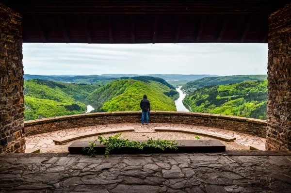 Aussichtsplattform über der Saarschleife Die Aussichtsplattform über der Saarschleife bei Mettlach am Tag mit einer Person die über den Fluss blickt.