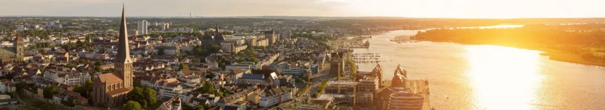 Die Skyline von Rostock bei Sonnenuntergang mit einem prägnanten Kirchturm und den zahlreichend Gebäuden im Herzen der Stadt an der Unterwarnow.