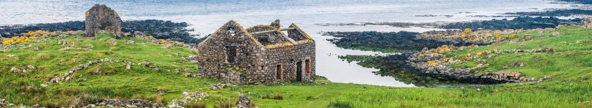 Eine alte steinerne Hausruine auf Rathlin inmitten einer Wiese die an das Meer angrenzt bei Tag.
