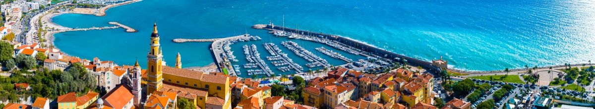 Küstenabschnitt von Menton mit Hafen und gelbem Kirchturm.