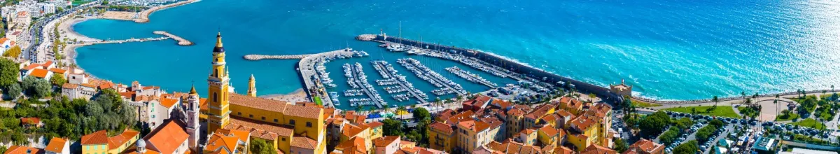 Küstenabschnitt von Menton mit Hafen und gelbem Kirchturm.