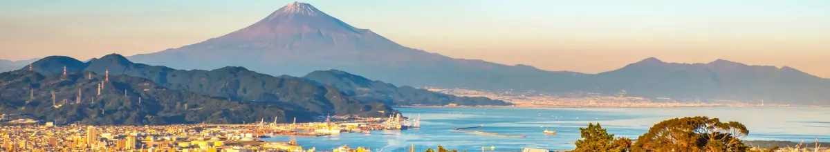 Die Sonne scheint auf die am Meer liegende Stadt Shimizu und den Berg Fuji.
