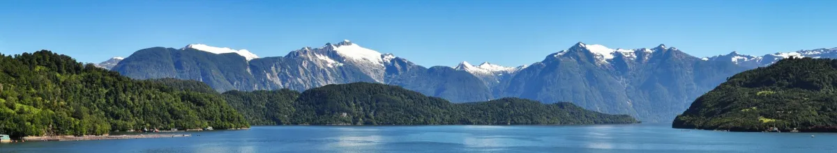 Berglandschaft und Fjorde am Wasser unter blauem Himmel.