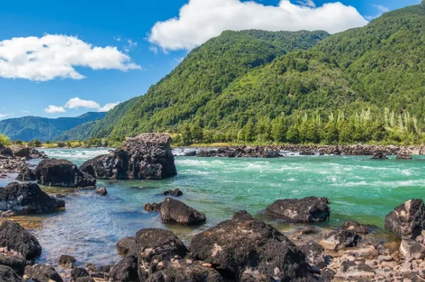 Puerto Chacabuco Türkisfarbener Fluss mit steiniger Felslandschaft im Vordergrund, im Hintergrund grüne Berglandschaft.
