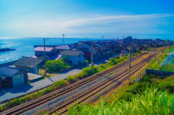 Alte Bahngleise, die sich durch Akita schlängeln bei Tag mit den Häusern der Stadt nebendran und dem Meer im Hintergrund bei Tag.