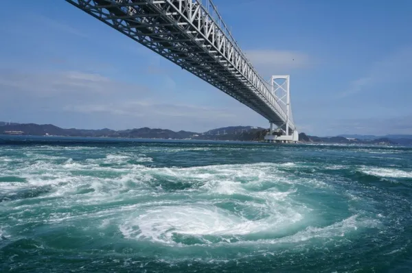 Großer Strudel in einer Meerenge, über die eine Brücke führt.