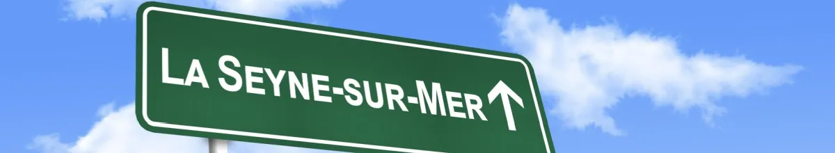 Ein grünes Ortsschild auf dem "La Seyne-sur-Mer" steht vor einem blauen Himmel.