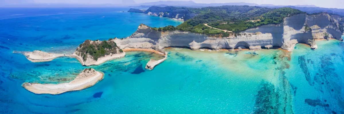 Panoramaansicht von Korfu mit weißen Felsen  an der Küste und bewaldeten Hängen im Hinterland.