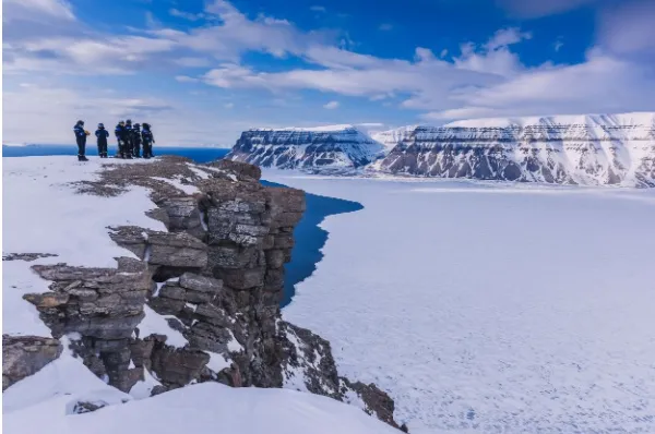 Eine Gruppe Reisender in Tempfelfjorden Eine Expeditionsgruppe in Tempelfjorden auf einem Bergmassiv, die über die eisige Landschaft schauen.