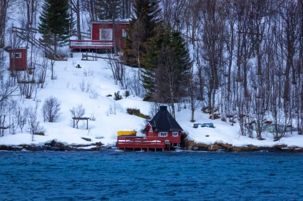 Ein Haus an Gibostads Küste Ein Häuschen in Gibostad am Wasser inmitten einer verschneiten Landschaft bei Tag.
