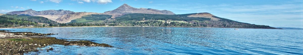 Panorama der felsigen Küstenlinie der Isle of Arran mit Berg im Hintergrund.