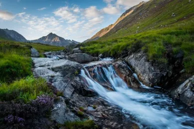 Kleiner Wasserfall am Fluss auf der Isle of Arran, der sich durch eine Wiesenlandschaft schlängelt.