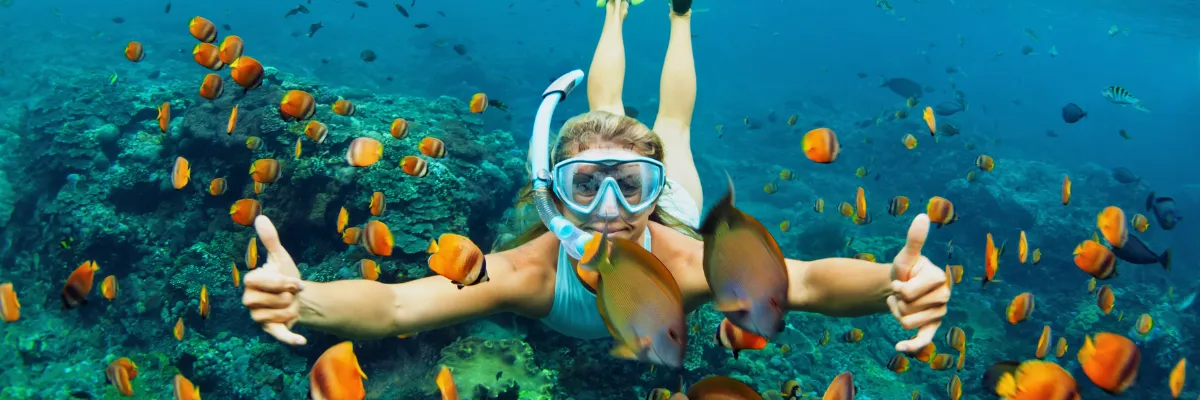 Eine Frau mit Taucherbrille und Schnorchel schwimmt mit kleinen Fischen bei den Bahamas.