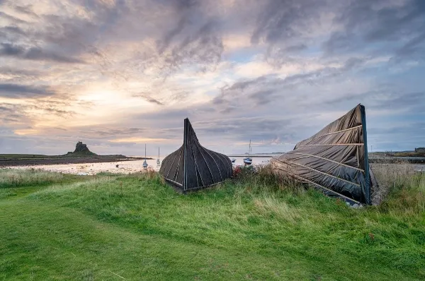 Zwei kleine Boote am Strand von Lindisfarne mit den Klosterruinen fern im Hintergrund.